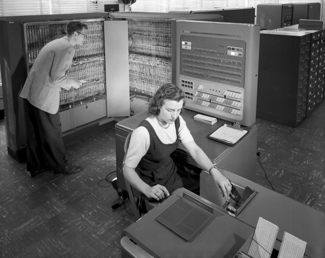 An old picture of a young man and woman shown working on an IBM 704 data machine.