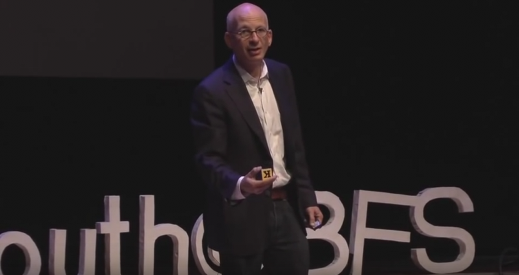 Picture of Seth Goden speakin on stage at Tedx Youth. He is holding a small alphabet block.