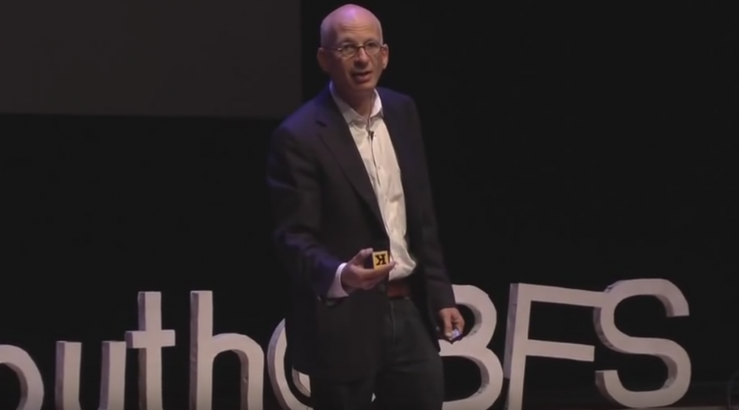 Picture of Seth Goden speakin on stage at Tedx Youth. He is holding a small alphabet block.